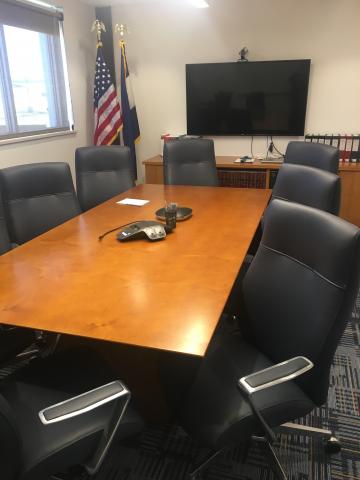 Conference desk with TV, telephone, total of 9 chairs and American and Colorado State flags.